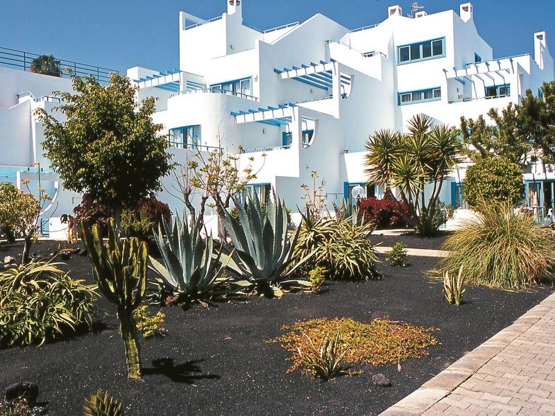Edificio dell'hotel bianco con vegetazione mediterranea e cielo blu limpido.