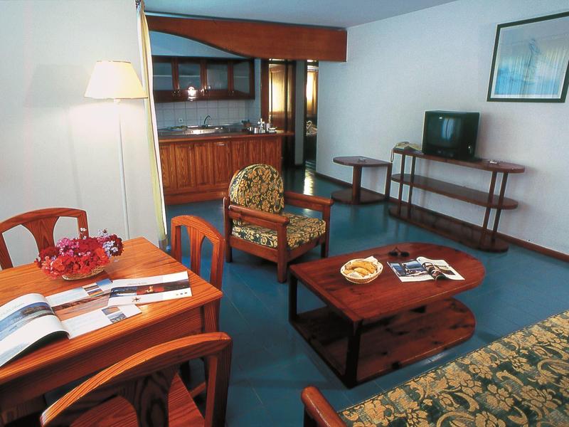 Camera d'hotel accogliente con tavolo, sedia, divano e TV su moquette blu.