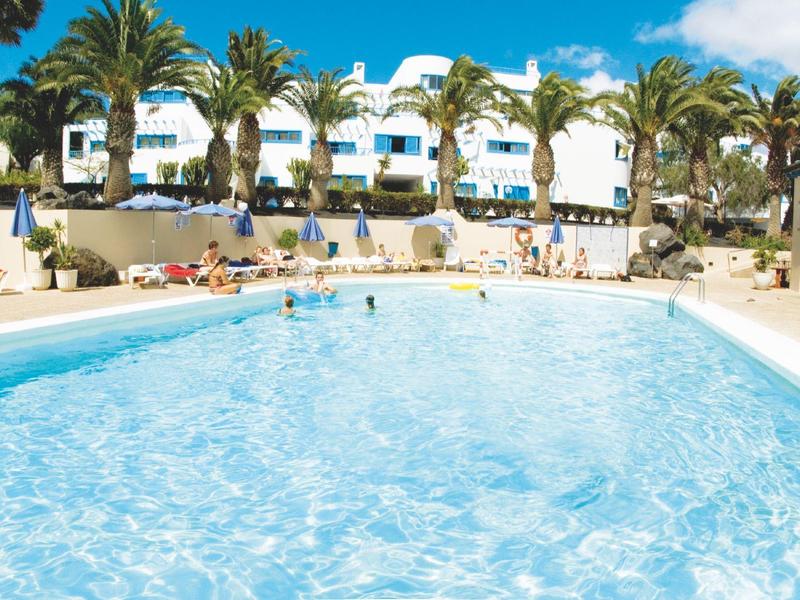 Piscina con acqua e ombrelloni davanti a un hotel con palme