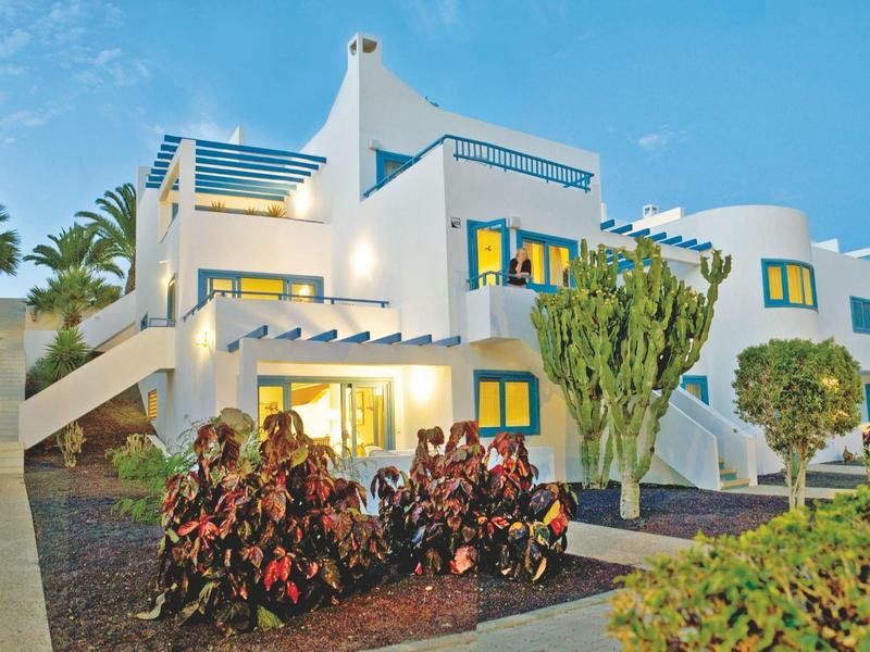 Casa vacanze bianca con terrazza e piante in una serata soleggiata.