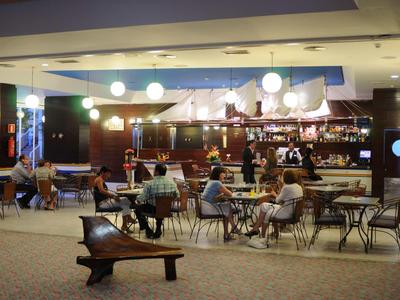 Innenraum eines Hotels mit Bar, Tischen und Gästen, die sitzen und sich unterhalten.