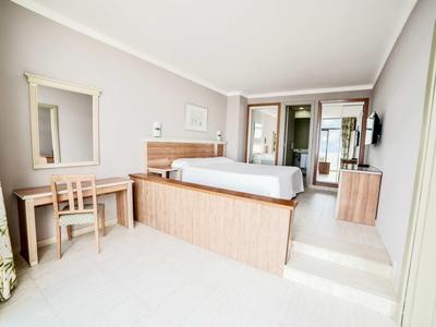 Camera d'hotel luminosa con letto matrimoniale, scrivania, TV e tende con motivo floreale.