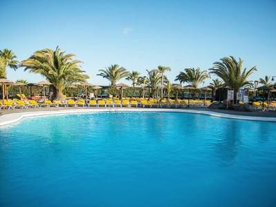 Großer blauer Pool mit Palmen, Sonnenschirmen und klar blauem Himmel im Hintergrund.