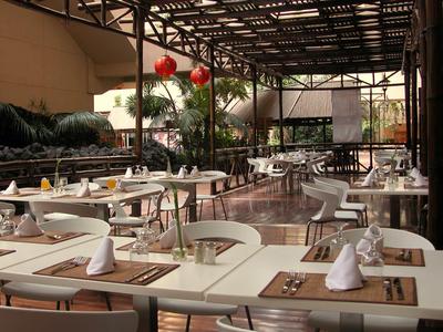 Überdachter Außenbereich eines Restaurants mit weißen Tischen und Stühlen, dekoriert mit Papierlampen.