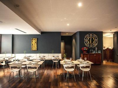 Moderner, eleganter Speiseraum mit Holzboden, weißen Tischen und Stühlen vor dunklen Wänden.