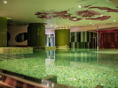 Piscina interna con acqua illuminata di verde e colonne nell'interno dell'hotel.