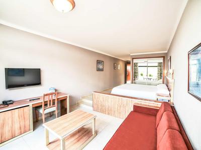 Camera d'hotel luminosa con letto matrimoniale, divano, scrivania e TV.