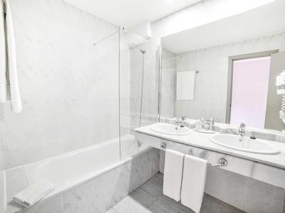 Bagno luminoso con vasca, grande specchio e asciugamani bianchi.