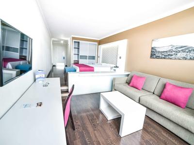 Camera d'hotel moderna con divano, TV e area lavoro in colori chiari.