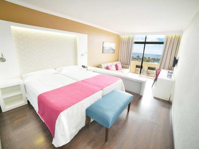 Camera d'hotel moderna con letto matrimoniale, pareti luminose e vista mare.