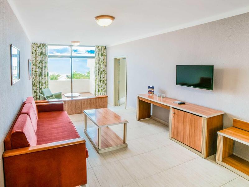 Soggiorno luminoso con divano, TV a parete e vista sull'area esterna con acqua