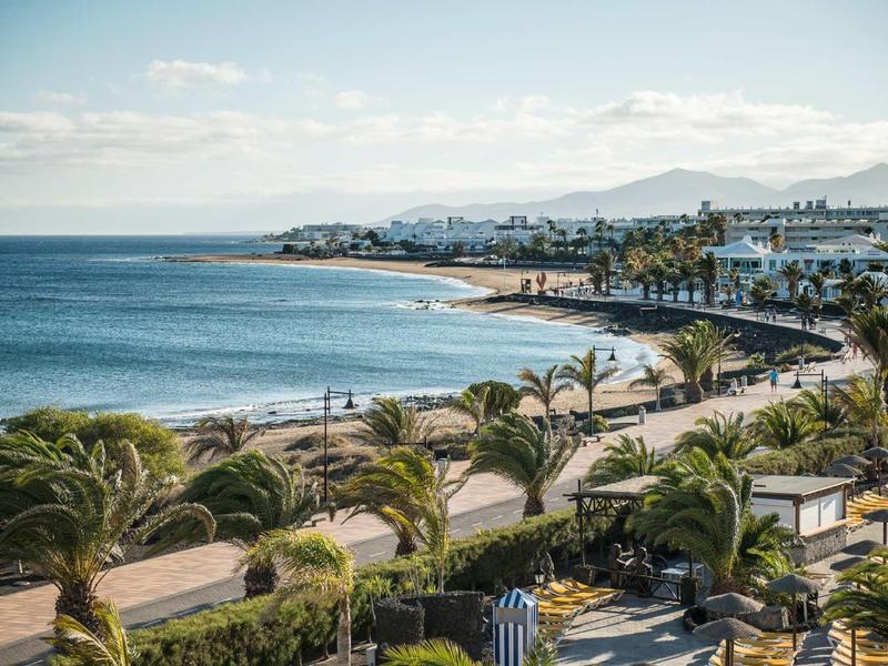 Paesaggio costiero con spiaggia, palme e hotel con tempo sereno.