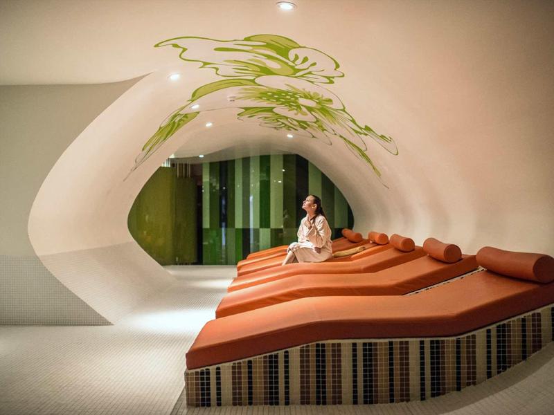 Sala relax moderna con lettini arancioni e design murale organico.