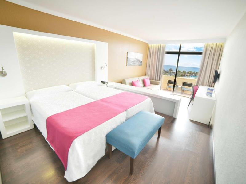 Camera d'hotel moderna con letto matrimoniale, pareti luminose e vista mare.