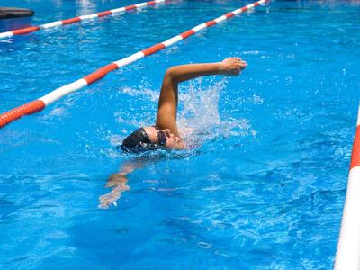 Eine Person schwimmt im blauen Wasser eines Schwimmbeckens zwischen roten und weißen Bahnen.