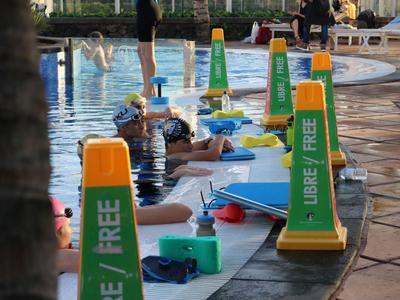 Schwimmbad mit Schwimmern, gelben Absperrkegeln und blauen Schwimmbrettern am Beckenrand.