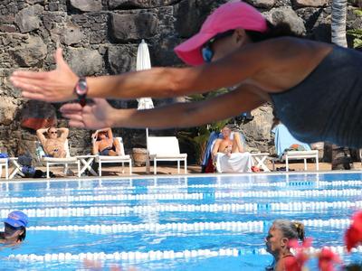 Frau springt in ein Schwimmbecken, im Hintergrund Zuschauer auf weißen Liegestühlen.