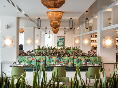 Moderní interiér hotelové restaurace se zelenými rostlinami a teplým osvětlením.