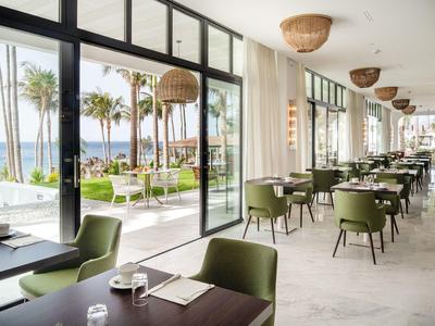 Moderner, heller Restaurantbereich mit grünen Stühlen, großen Fenstern und Meerblick.