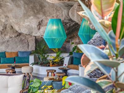 Gemütliche Lounge mit blauen Lampen, Holzmöbeln und üppiger Pflanzendekoration in felsiger Umgebung.