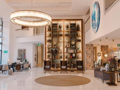 Heller Hotel-Lobbybereich mit großzügiger Sitzecke, runder Deckenleuchte und dekorativem Wandregal.