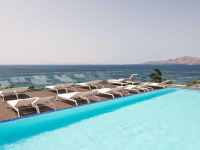 Ein Pool mit blauer Wasseroberfläche, Liegestühle, Meer und kühlender Himmel im Hintergrund.