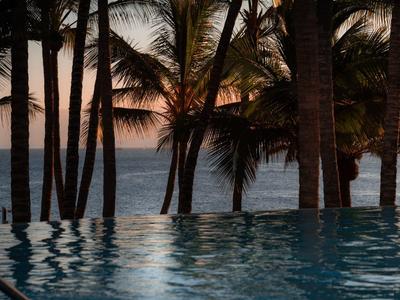 Palm Bäume am Meer bei Sonnenuntergang mit einem ruhigen Wasserbecken im Vordergrund.