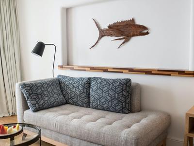 Moderner Wohnraum mit grauem Sofa, zwei gemusterten Kissen, schwarzer Lampe und Holzfisch an der Wand.