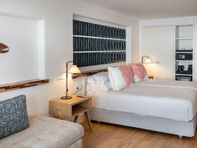 Modernes Zimmer mit zwei weißen Betten, Holzsideboard, grauem Sofa und dunkler Wandkunst.