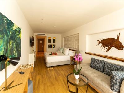 Moderner Hotelzimmer mit Holzboden, Doppelbett, Sofa, großem Bild an der Wand und Pflanzen auf Tischen.