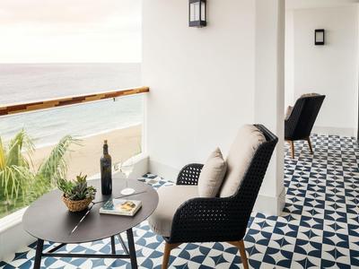 Heller Balkon mit gemusterter Fliese, schwarzem Tisch, Stühlen und Blick aufs Meer und Palmen.