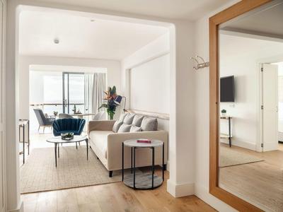 Helles Wohnzimmer mit grauem Sofa, großem Wandspiegel und Balkon mit Blick auf Stadt und Wasser.
