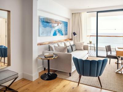 Helles Wohnzimmer mit grauem Sofa, blauer Sessel, Holzboden und Meerblick durch große Fenster.