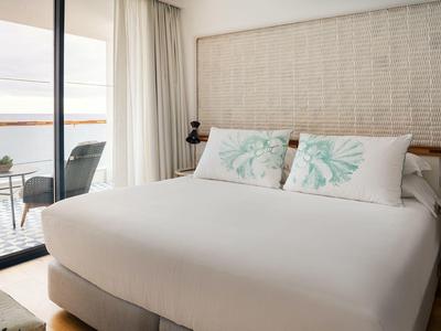 Helles, modernes Schlafzimmer mit großem Bett, zwei Kissen mit Blattmuster und Balkon mit Meerblick.
