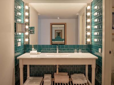 Modernes Badezimmer mit grün gekachelter Wand, großem Spiegel und zwei Waschbecken auf weißem Tisch.