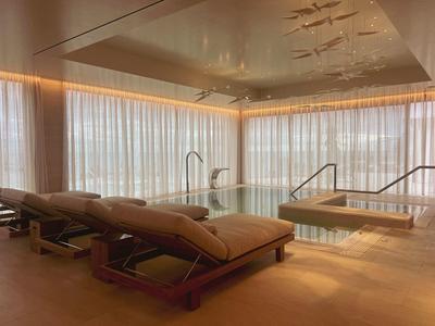 Modernes Hallenbad mit großen Fenstern, Lounge-Stühlen und ruhiger LED-Beleuchtung in warmen Tönen.