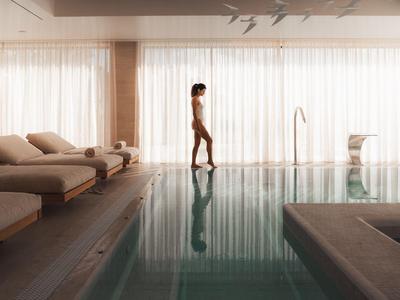 Person walking barefoot beside an indoor pool in a modern wellness area.