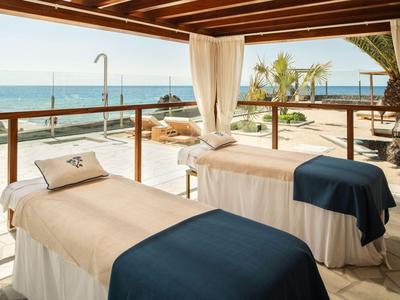 Two massage beds on a terrace with ocean view and soft curtains.