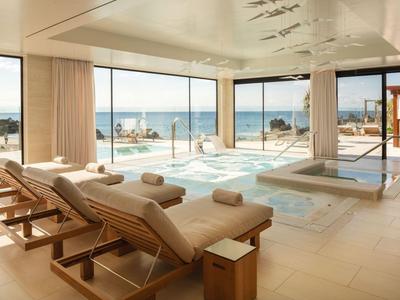 Bright spa lounge with lounge chairs and sea view through large windows.