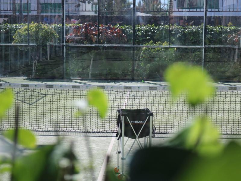 Sedia vuota davanti a un campo da tennis, circondata da piante verdi.
