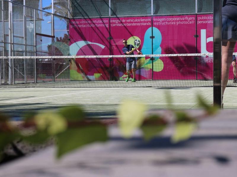 Vista di un campo da tennis con giocatori in movimento e muro colorato sullo sfondo.