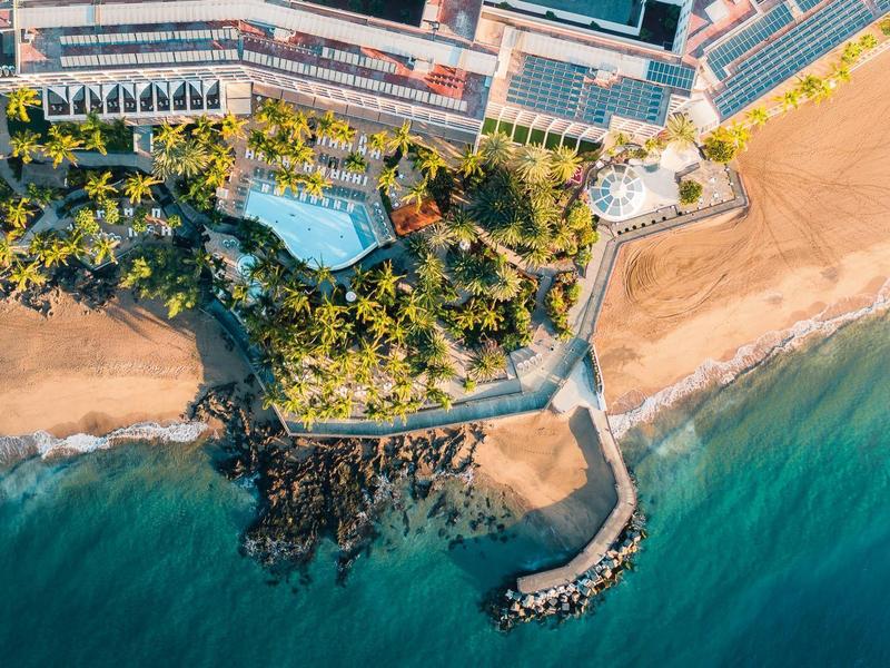 Veduta aerea di un hotel con piscina, palme, spiaggia e molo sul mare