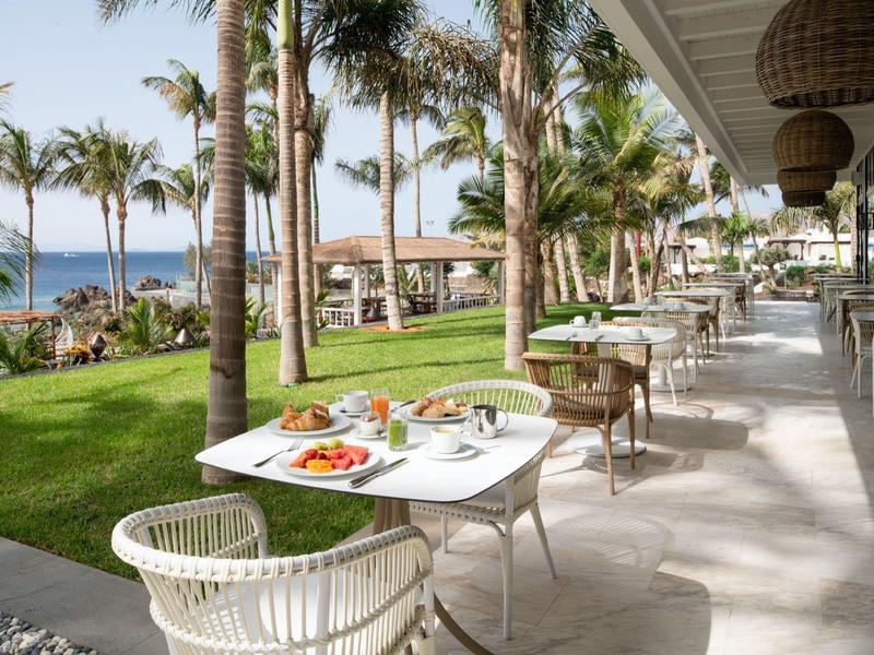 Terrazza del ristorante con tavoli, sedie e vista sul mare circondato da palme.
