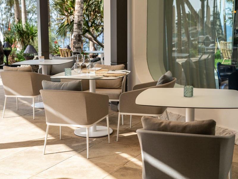 Terrazza luminosa con tavoli e sedie moderne, circondata da finestre di vetro e piante.