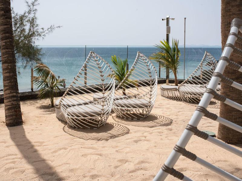 Poltrone in vimini moderne e amache su spiaggia sabbiosa con vista sul mare e palme.