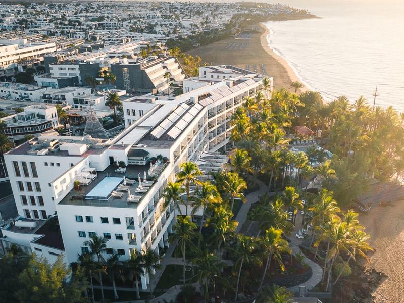 Vista di un hotel sulla costa con palme e spiaggia adiacente al tramonto.