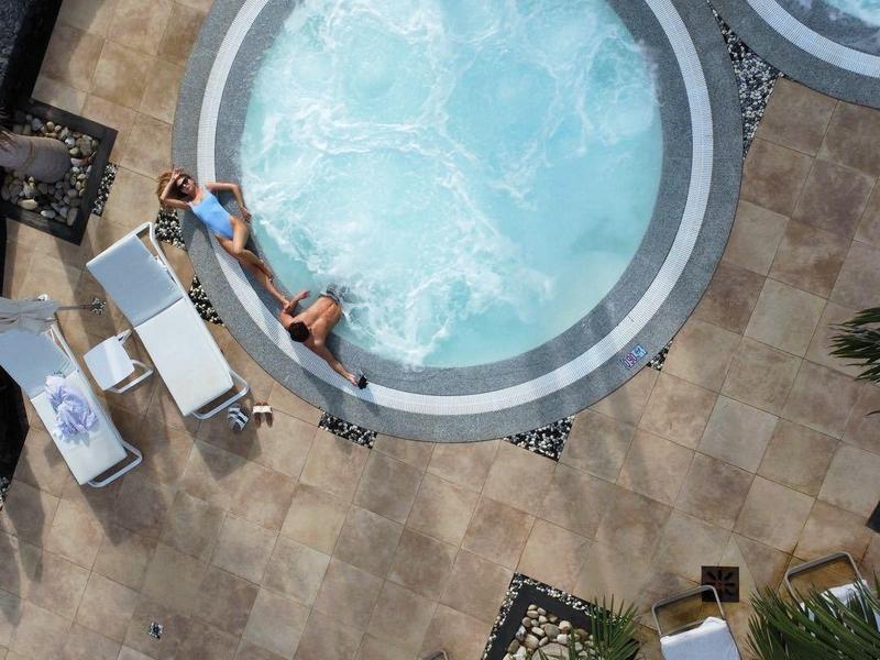 Due vasche idromassaggio rotonde su una terrazza con lettini e palme.