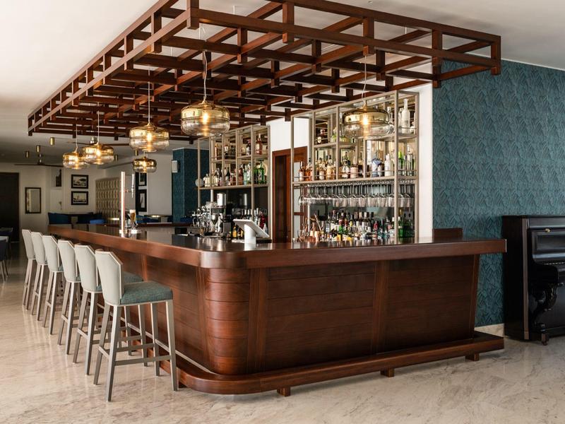 Bar d'hotel elegante con bancone in legno, sgabelli grigi e luci sospese.