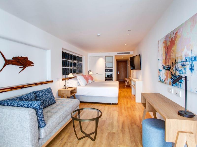 Camera d'hotel moderna con divano, letto matrimoniale e opere d'arte alle pareti.