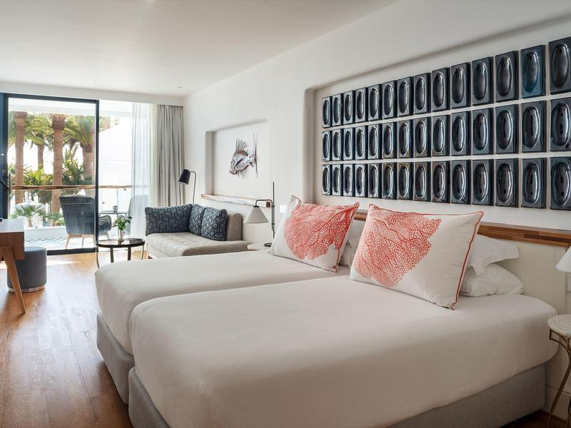 Camera d'hotel moderna con due letti singoli, cuscini rosa e accesso a una terrazza esterna.